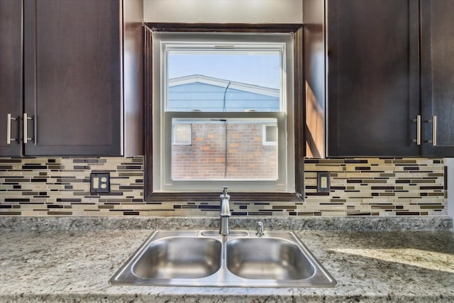 kitchen with light stone countertops, sink, dark brown cabinets, and backsplash