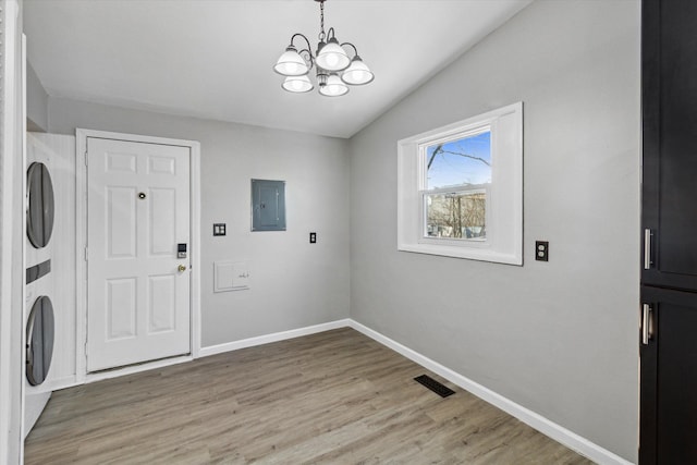 laundry room with stacked washer / dryer, electric panel, light hardwood / wood-style flooring, and a notable chandelier