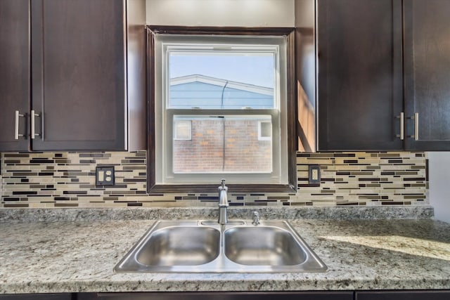 kitchen featuring light stone counters, dark brown cabinets, sink, and decorative backsplash