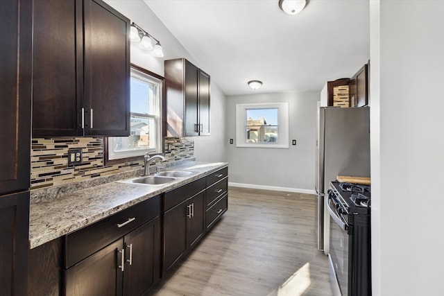 kitchen featuring dark brown cabinetry, sink, gas range, tasteful backsplash, and light wood-type flooring