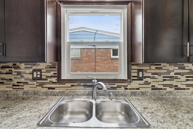 kitchen with tasteful backsplash, light stone countertops, sink, and dark brown cabinets