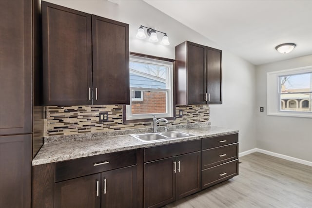 kitchen featuring vaulted ceiling, sink, decorative backsplash, dark brown cabinetry, and light hardwood / wood-style flooring