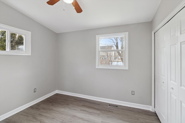 unfurnished bedroom with multiple windows, hardwood / wood-style floors, ceiling fan, and a closet