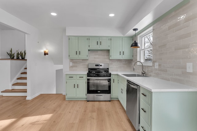 kitchen featuring sink, backsplash, stainless steel appliances, green cabinetry, and decorative light fixtures