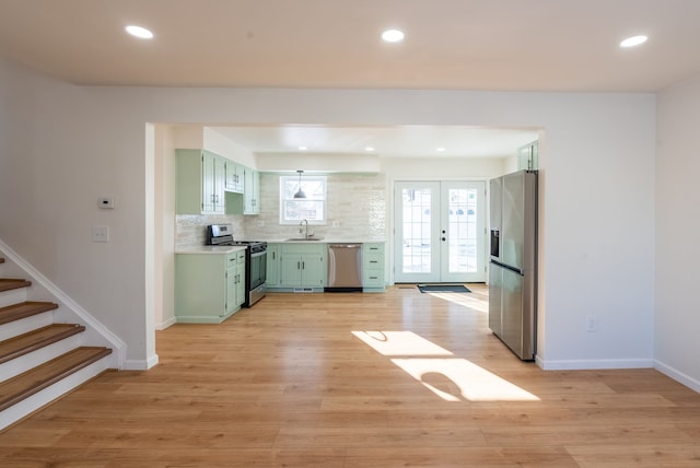 kitchen with appliances with stainless steel finishes, sink, green cabinets, light wood-type flooring, and french doors