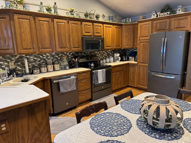 kitchen featuring sink, light hardwood / wood-style flooring, stainless steel appliances, tasteful backsplash, and vaulted ceiling