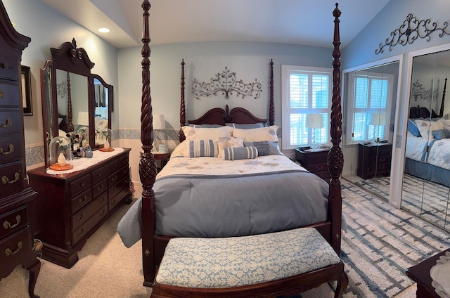 bedroom with multiple closets, vaulted ceiling, and light colored carpet