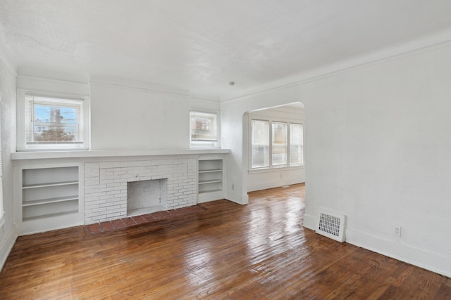 unfurnished living room with wood-type flooring, a brick fireplace, a healthy amount of sunlight, and built in shelves