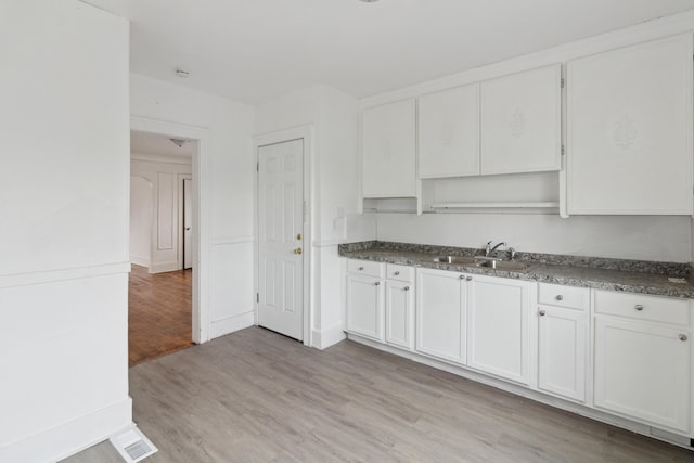 kitchen featuring white cabinets, dark stone countertops, sink, and light wood-type flooring