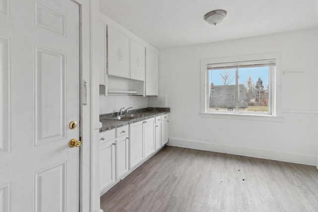 kitchen featuring white cabinetry, light hardwood / wood-style floors, sink, and dark stone countertops