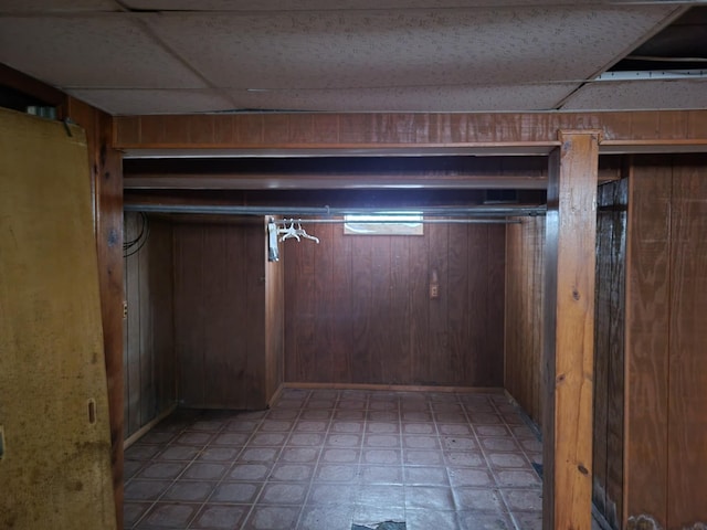 basement featuring a paneled ceiling and wooden walls