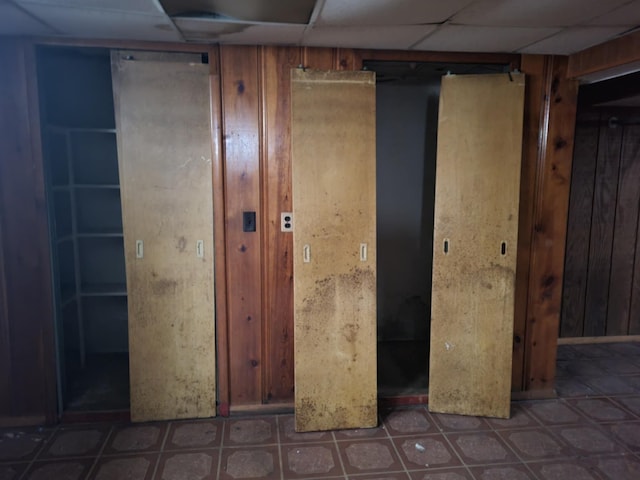 basement featuring a drop ceiling and wood walls