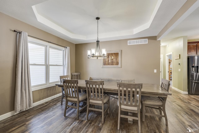 dining area featuring an inviting chandelier, a tray ceiling, and dark hardwood / wood-style flooring