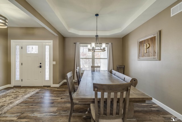 dining space featuring a notable chandelier, a tray ceiling, and dark wood-type flooring