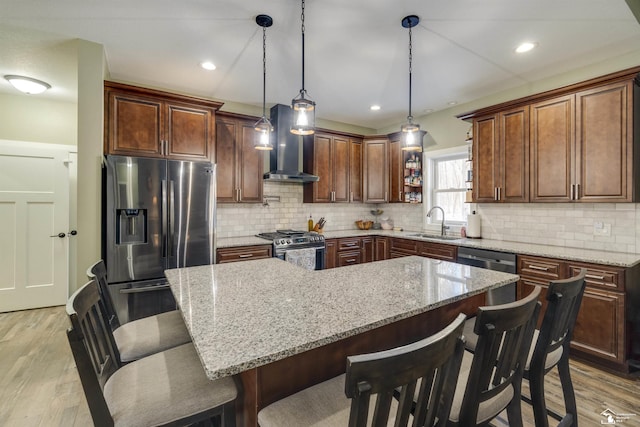 kitchen with sink, appliances with stainless steel finishes, a kitchen island, decorative light fixtures, and wall chimney exhaust hood