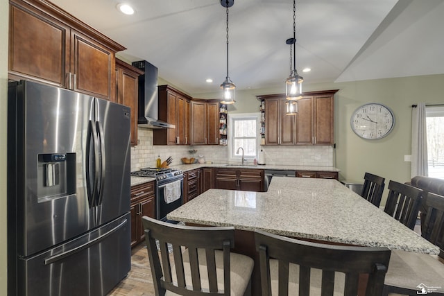 kitchen with appliances with stainless steel finishes, a breakfast bar, hanging light fixtures, a center island, and wall chimney range hood