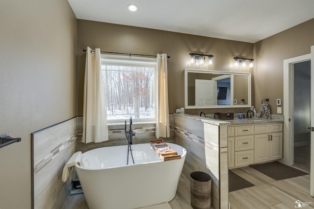 bathroom featuring vanity, a bath, hardwood / wood-style floors, and tile walls