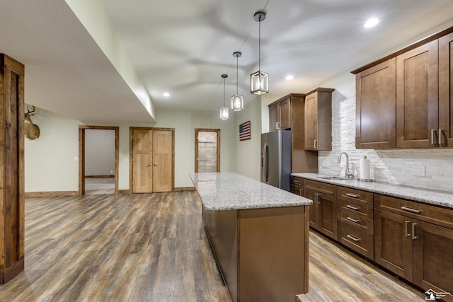 kitchen with light stone countertops, a kitchen island, sink, and stainless steel fridge with ice dispenser