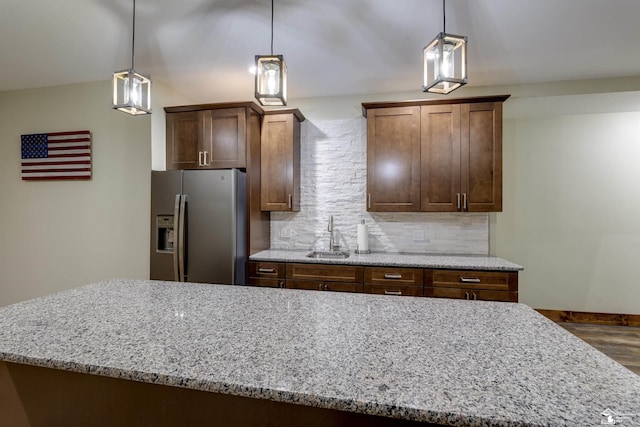 kitchen with decorative light fixtures, tasteful backsplash, sink, stainless steel fridge, and light stone countertops