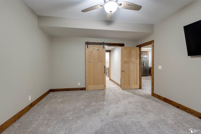 unfurnished bedroom featuring stainless steel refrigerator with ice dispenser, a barn door, light carpet, and ceiling fan