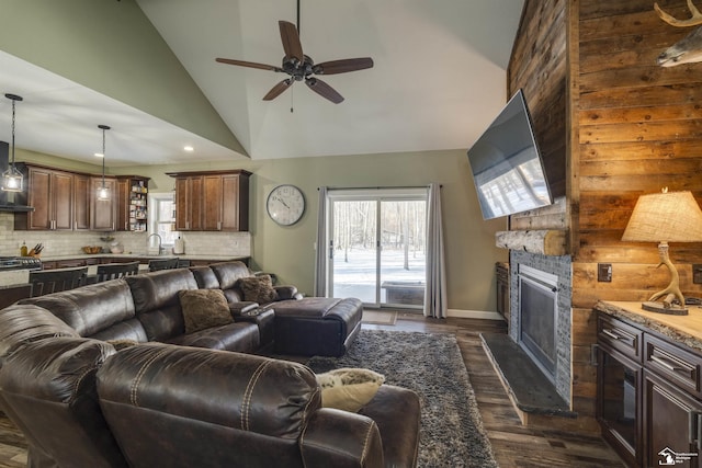 living room featuring sink, dark wood-type flooring, ceiling fan, high vaulted ceiling, and a stone fireplace