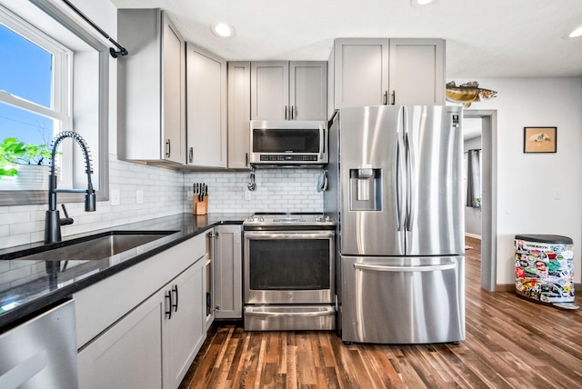 kitchen with tasteful backsplash, appliances with stainless steel finishes, gray cabinets, and dark stone counters