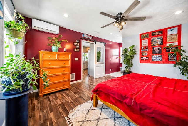 bedroom with a wall mounted air conditioner, ceiling fan, a barn door, dark wood-type flooring, and a textured ceiling