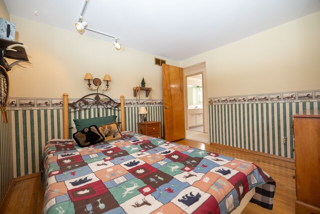 bedroom with track lighting, wood-type flooring, and ensuite bath