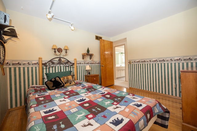 bedroom featuring ensuite bathroom, hardwood / wood-style floors, and track lighting