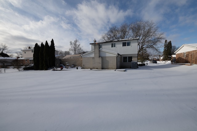 snow covered rear of property featuring central AC unit