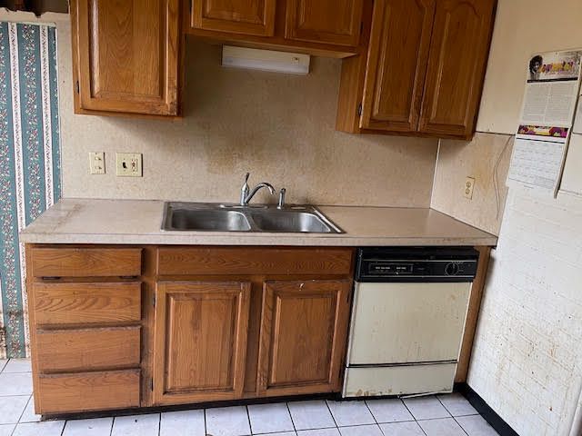 kitchen with brick wall, dishwasher, sink, and light tile patterned floors