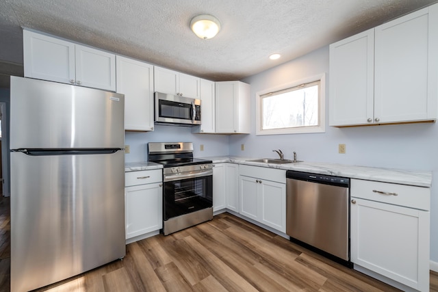 kitchen featuring sink, light stone counters, light hardwood / wood-style flooring, stainless steel appliances, and white cabinets