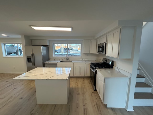 kitchen with sink, light stone counters, a kitchen island, stainless steel appliances, and light hardwood / wood-style floors