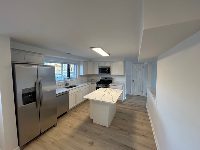 kitchen featuring a kitchen island, appliances with stainless steel finishes, white cabinetry, sink, and light stone counters