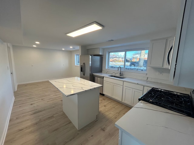 kitchen featuring appliances with stainless steel finishes, sink, a center island, light stone counters, and light hardwood / wood-style floors