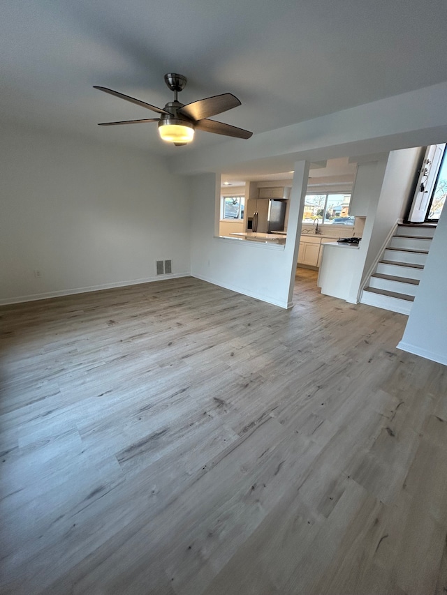 unfurnished living room with ceiling fan, sink, and light wood-type flooring