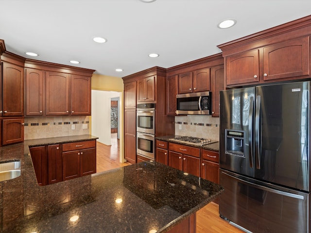 kitchen featuring dark stone countertops, backsplash, stainless steel appliances, and light hardwood / wood-style floors