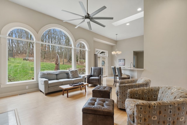 living room with sink, ceiling fan with notable chandelier, light wood-type flooring, and a skylight