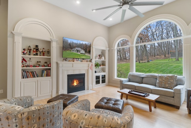 living room with a fireplace, built in features, light hardwood / wood-style floors, and a healthy amount of sunlight