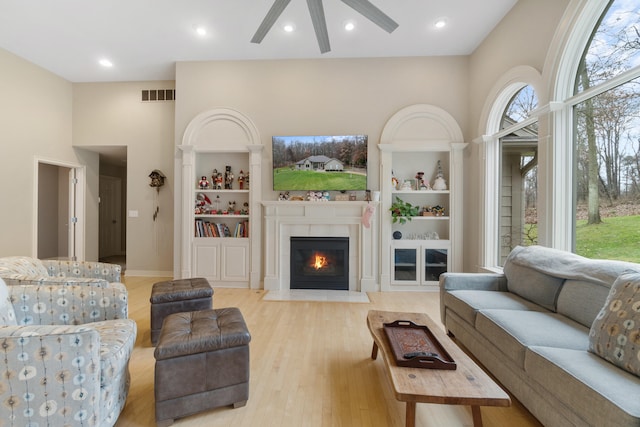 living room featuring ceiling fan, a tile fireplace, built in features, and light wood-type flooring