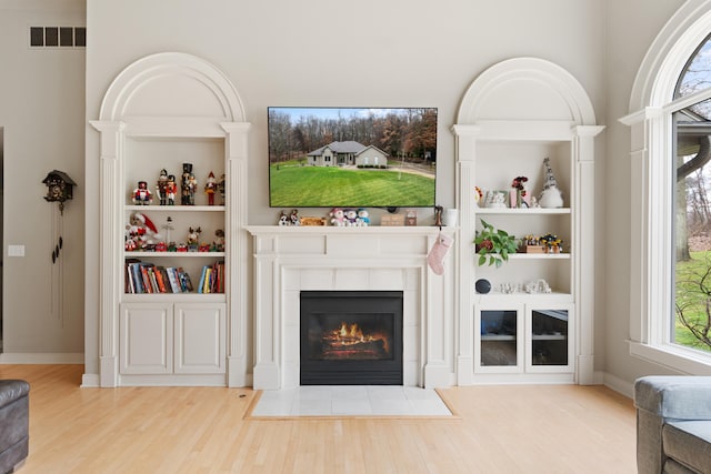 living room featuring a tiled fireplace, hardwood / wood-style floors, and built in features