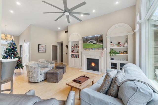 living room with built in shelves, high vaulted ceiling, ceiling fan, and light wood-type flooring