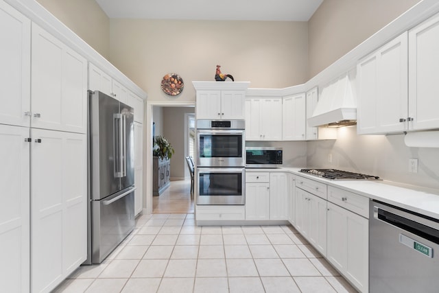 kitchen with white cabinetry, stainless steel appliances, light tile patterned flooring, and custom range hood