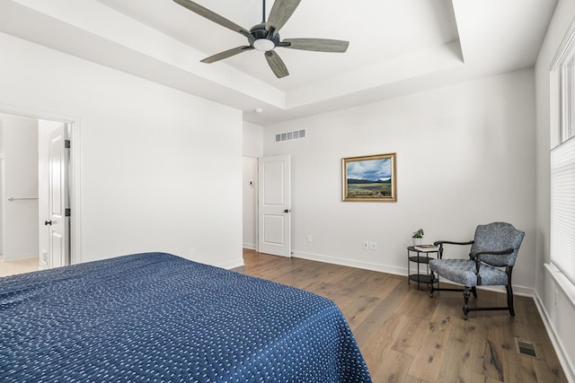 bedroom with hardwood / wood-style flooring, ceiling fan, and a tray ceiling