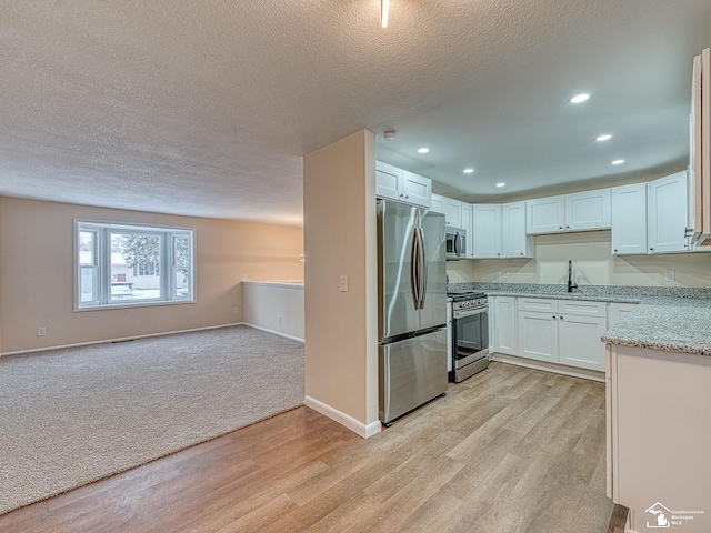 kitchen featuring sink, stainless steel appliances, light stone counters, white cabinets, and light wood-type flooring