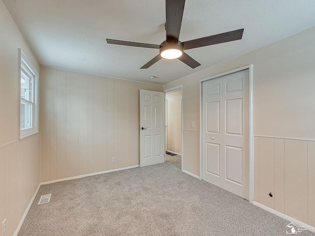 unfurnished bedroom with ceiling fan, light carpet, and wood walls