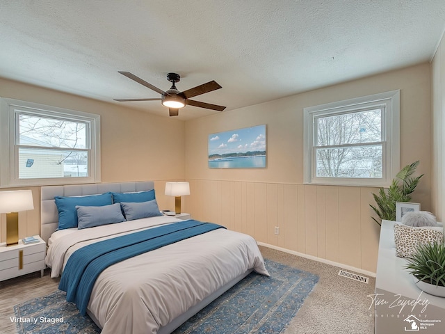 bedroom with a textured ceiling, ceiling fan, and wood walls