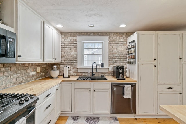 kitchen with sink, butcher block countertops, white cabinetry, stainless steel appliances, and light hardwood / wood-style floors