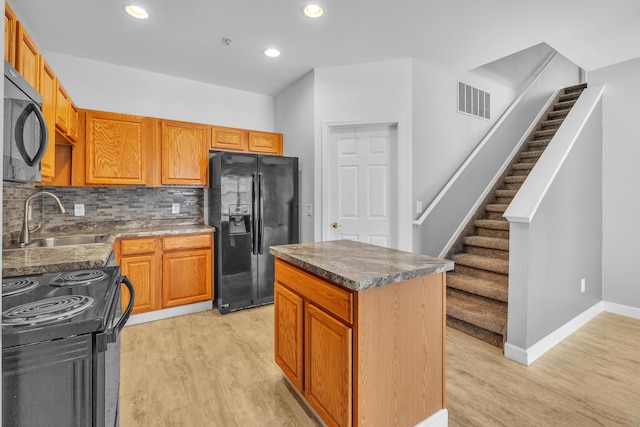 kitchen with sink, black appliances, a kitchen island, decorative backsplash, and light wood-type flooring