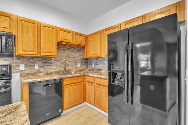 kitchen featuring sink, backsplash, light stone counters, black appliances, and light hardwood / wood-style flooring